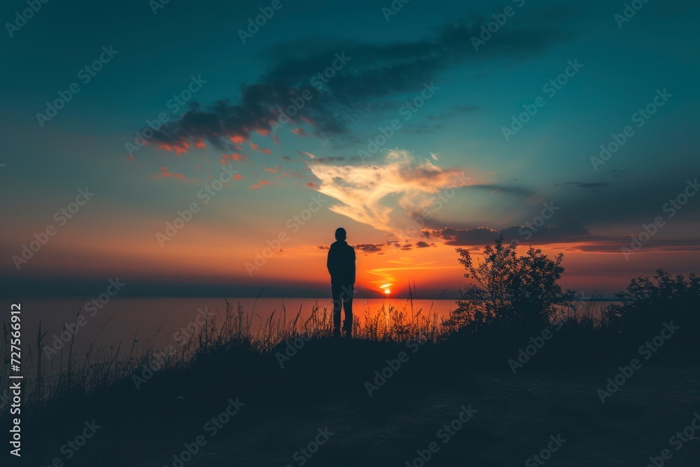 a man standing on a field looking away at the lagoon lake at twilight sunset