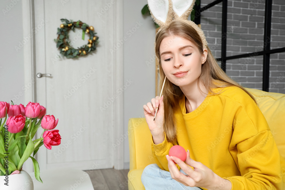 Young woman in bunny ears painting Easter egg at home Young woman in bunny ears painting Easter egg at home