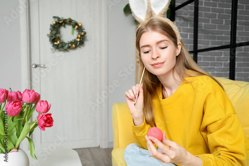Young woman in bunny ears painting Easter egg at home