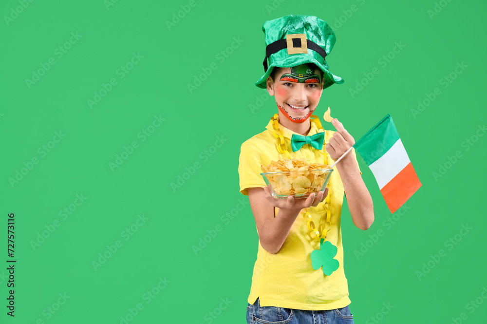 Funny boy with face painting, leprechaun's hat, Ireland flag and potato chips on green background. St. Patrick's Day celebration
