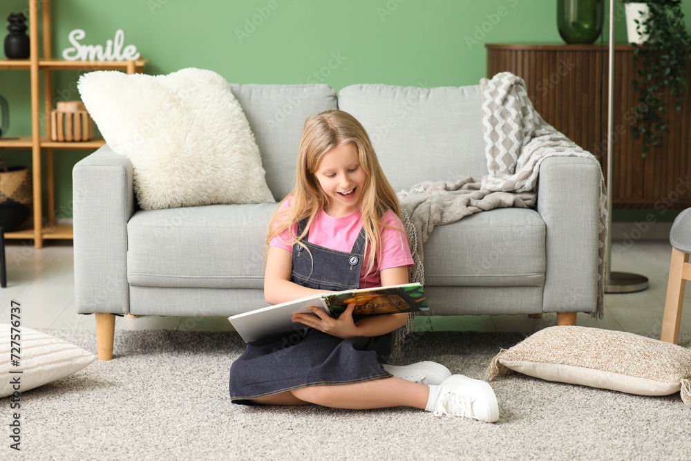 Cute little girl reading book while sitting on floor at home