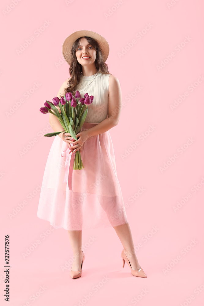 Happy young woman with bouquet of beautiful purple tulips on pink background