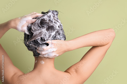 Young woman applying shampoo on green background, back view