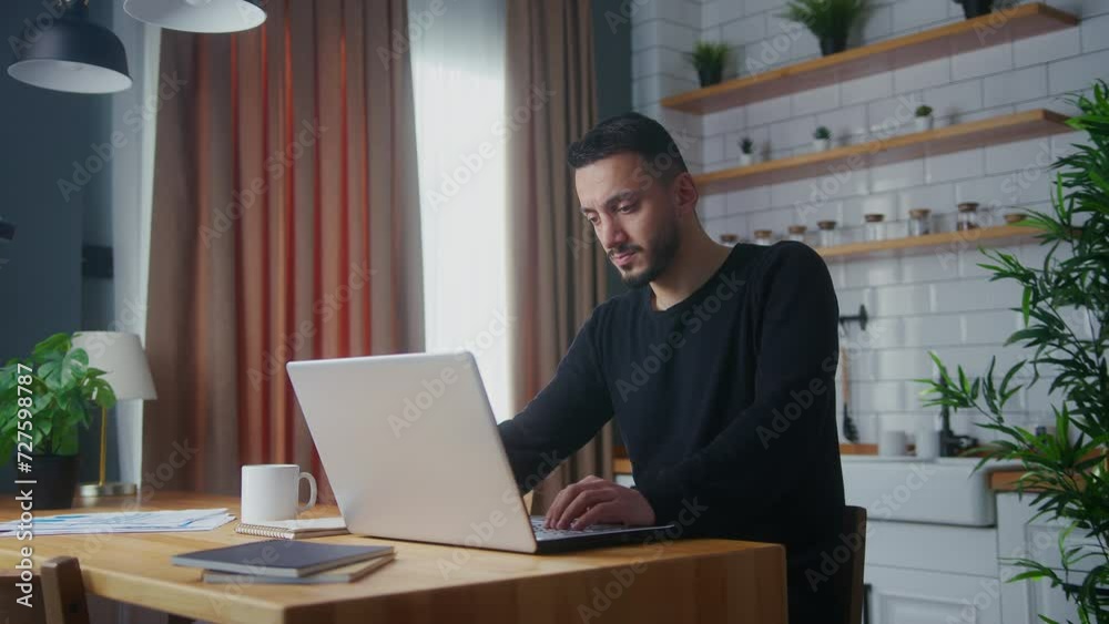 Adult man work at home in the kitchen working with his laptop, taking notes, doing research. Busy freelancer working on modern tech notebook device Adult man work at home in the kitchen working with his laptop, taking notes, doing research. Busy freelancer working on modern tech notebook device