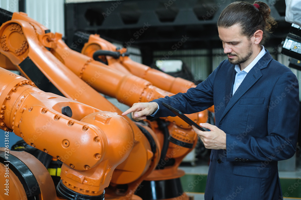 Bearded male engineer using tablet to check the number of automatic welding robot arms in industrial robot factory. Bearded male engineer using tablet to check the number of automatic welding robot arms in industrial robot factory.