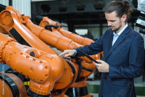 Bearded male engineer using tablet to check the number of automatic welding robot arms in industrial robot factory. © Nunkung