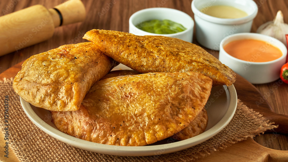 green empanadas in a bowl with sauces on a wooden table