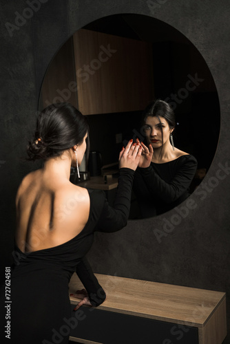 Sexy woman in a black dress posing near a mirror in a dark room. Fashion shooting concept