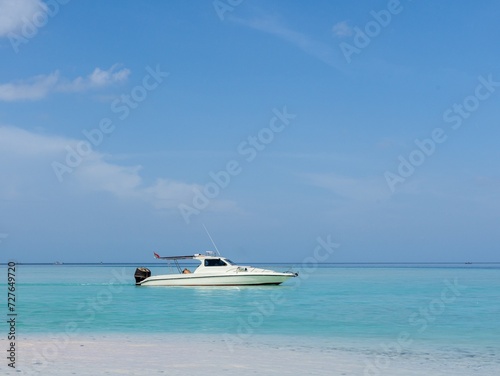 A small white speedboat anchored in the middle of turquoise water near a white sand beach. © DS Showcase