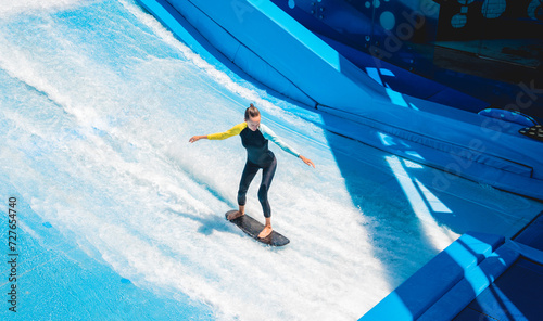 Canvas Print Beautiful young woman surfing on a wave simulator at a water amusement park