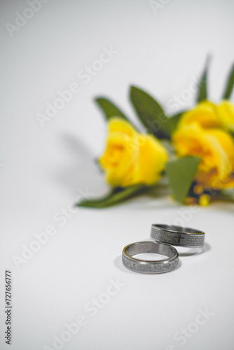 Silver rings with a cross in a white isolation background and yellow flowers.