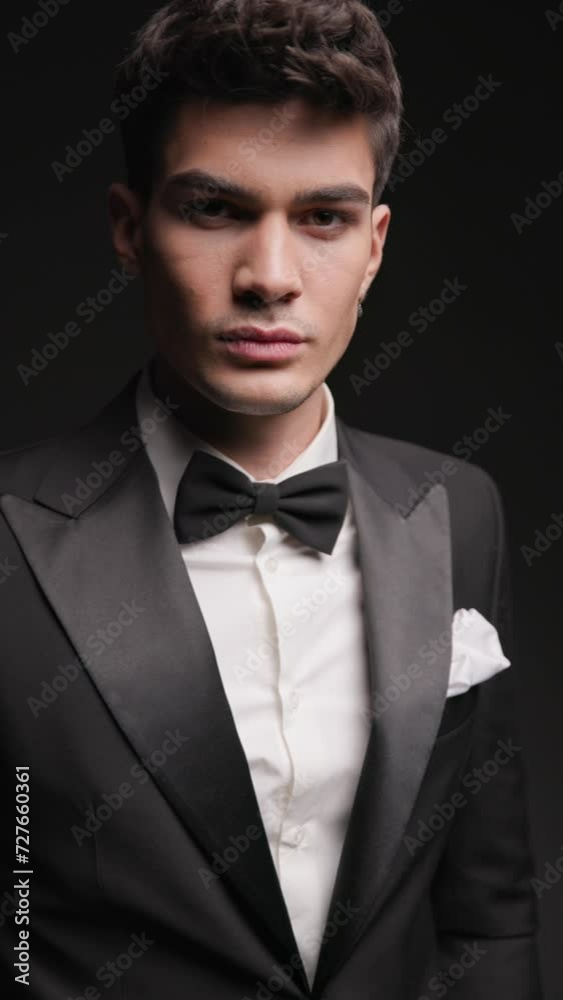 closeup of gentleman wearing black tux standing while holding pockets and looking down to side on dark background with strobes closeup of gentleman wearing black tux standing while holding pockets and looking down to side on dark background with strobes
