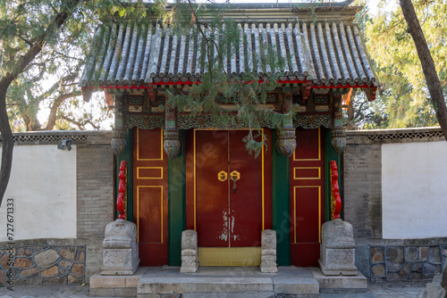 фотографія A traditional Chinese gate with concrete roof and densely ornamental upper section, two doors with golden circular knob, golden linings, and green pillars