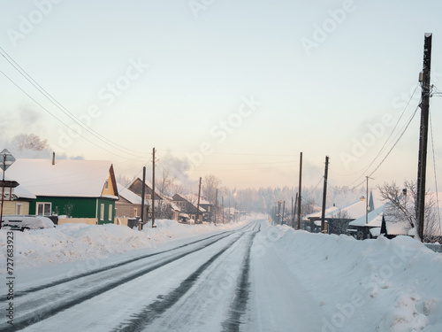 Winter road through a snow-covered village, severe frost, snow haze