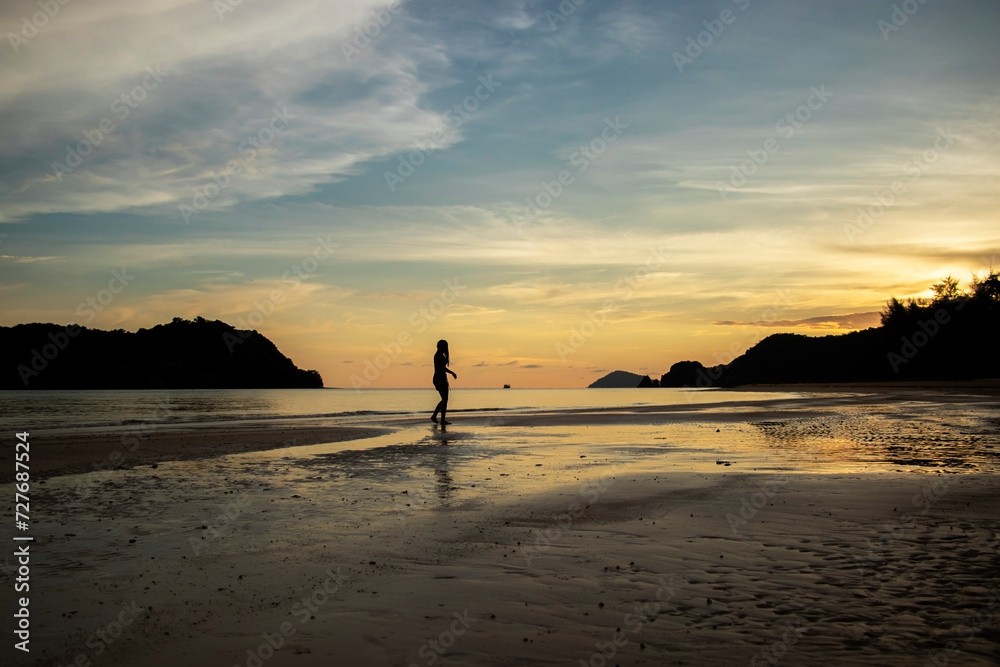 one silhouette of a woman walking on the beach at sunset