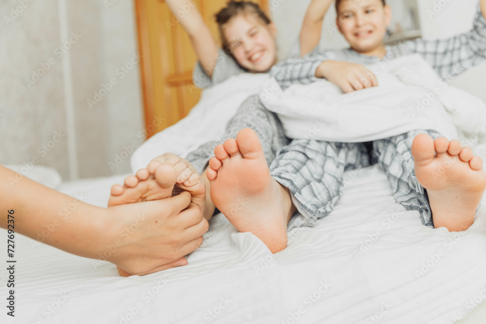 the children are wrapped in a blanket and tickling each other's heels on the bed. Family having fun at home. Leisure