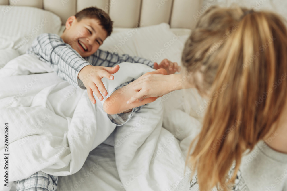 the children are wrapped in a blanket and tickling each other's heels on the bed. Family having fun at home. Leisure the children are wrapped in a blanket and tickling each other's heels on the bed. Family having fun at home. Leisure