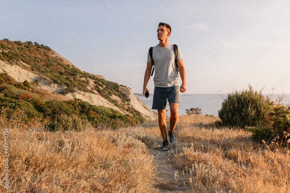Handsome man with backpack walking on the ocean coastline with mountains and evening warm sunlight. Handsome man with backpack walking on the ocean coastline with mountains and evening warm sunlight.