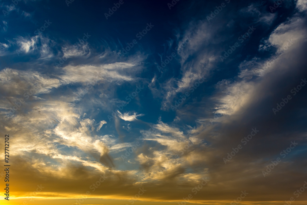 Fototapeta premium Cumulostratus, Stratus and Altocumulus clouds at golden hour in the blue sky lit by the sun at sunset or sunrise. Morning or evening, winter or summer. Blue and yellow gradient in the sky.