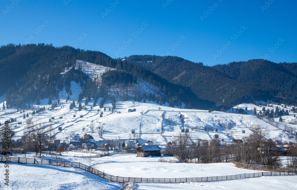 Landscape with a mountain village in winter. Houses spread out on a slope in the countryside covered with snow