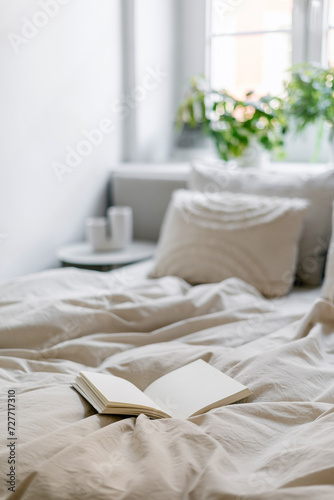 Open paper notebook on bed with blanket and pillows in cozy bedroom