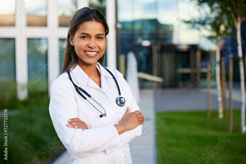 Confident trustworthy female doctor wearing lab coat with stethoscope standing outside modern hospital clinic