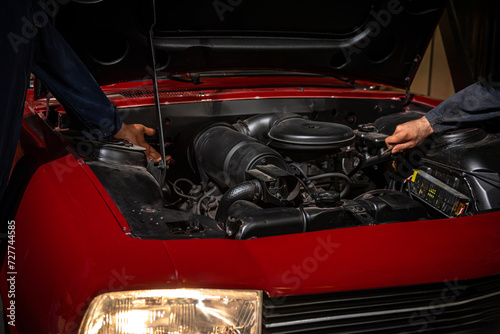 Two mechanics repair and maintain the engine of a red car
