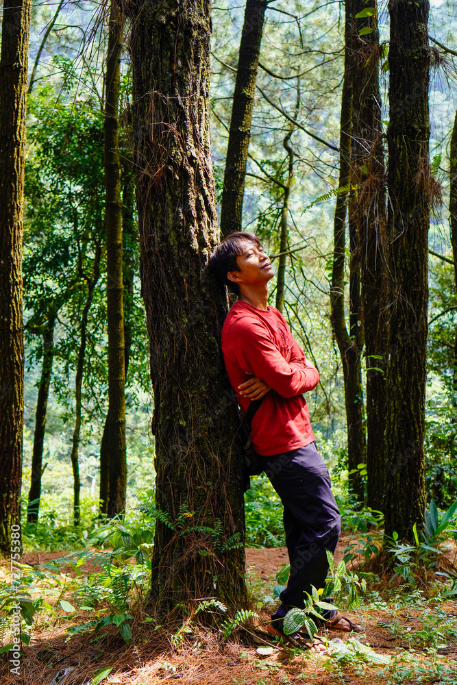 Javanese man in red is leaning against a tree in the forest. Javanese man in red is leaning against a tree in the forest.