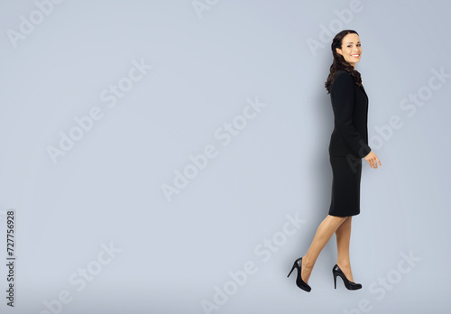 Full body length profile side photo of happy excited smiling businesswoman going side away, copy space area. Waking confident business woman wear black suit, isolated on grey gray background.
