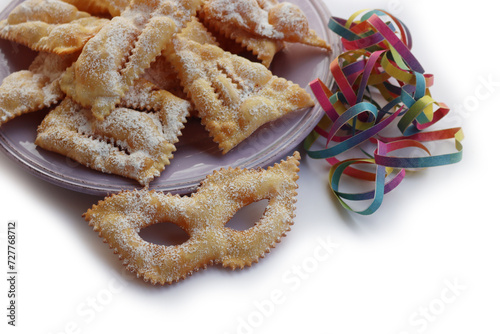 Italian sweet crisp pastry deep-fried and sprinkled with sugar in shape of Carnival mask on colorful plates on white. Chiacchere or crostoli, bugie, cenci with confetti and paper serpentine photo