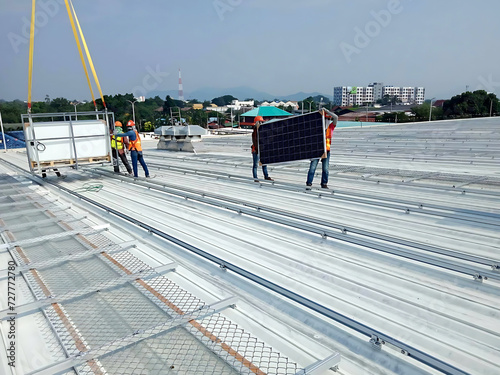 The Photovoltaic solar panels transported by the Crane trucks and workers at the rooftop of a factory building
