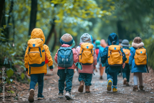 Group of primary school students with backpacks and raincoats go on an excursion with the school, walking through the forest.