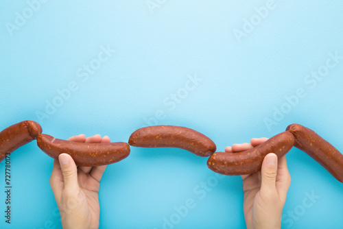 Young adult woman hands holding and showing string of raw fresh thick sausages for frying. Light blue table background. Pastel color. Closeup. Point of view shot. Top down view. photo