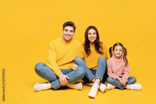 Full body young smiling happy cheerful parents mom dad with child kid girl 7-8 years old wear pink sweater casual clothes sitting look camera isolated on plain yellow background. Family day concept.