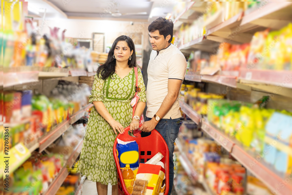 Indian couple shopping for groceries at the supermarket. Buying grocery for home. Couple checking products in grocery store.