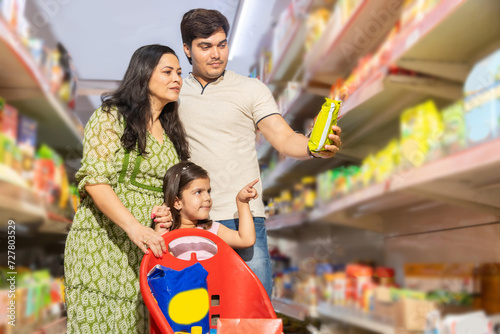 Happy indian family shopping for groceries at the supermarket. Man holding, checking the product details and little girl pointing at the products.