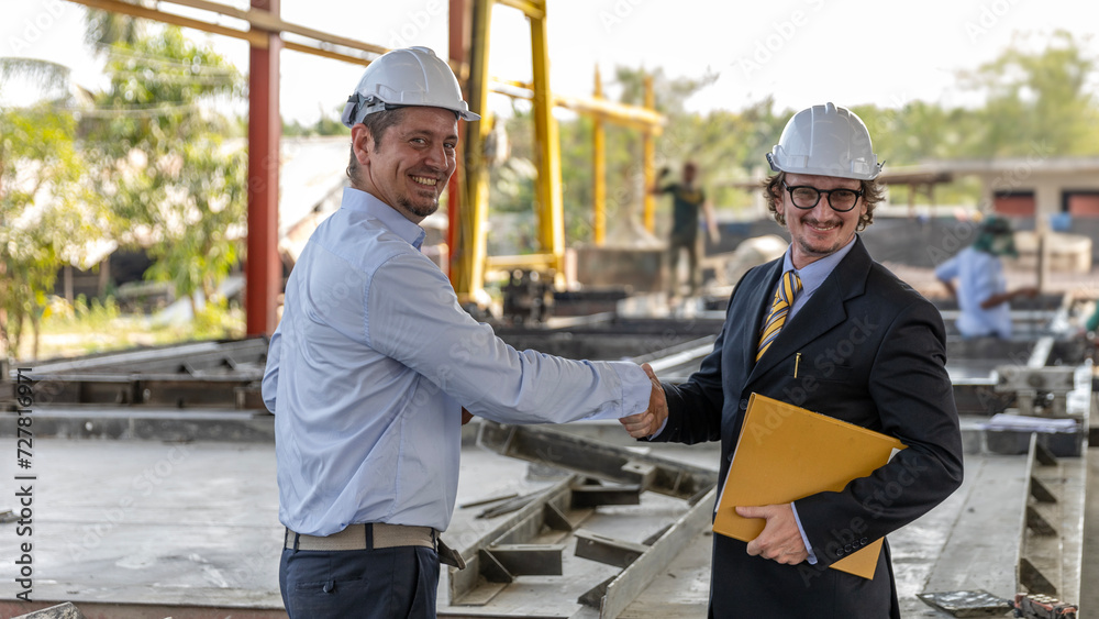 Two civil engineers from different cultures reach partnership agreement and have handshake in a construction factory Two civil engineers from different cultures reach partnership agreement and have handshake in a construction factory