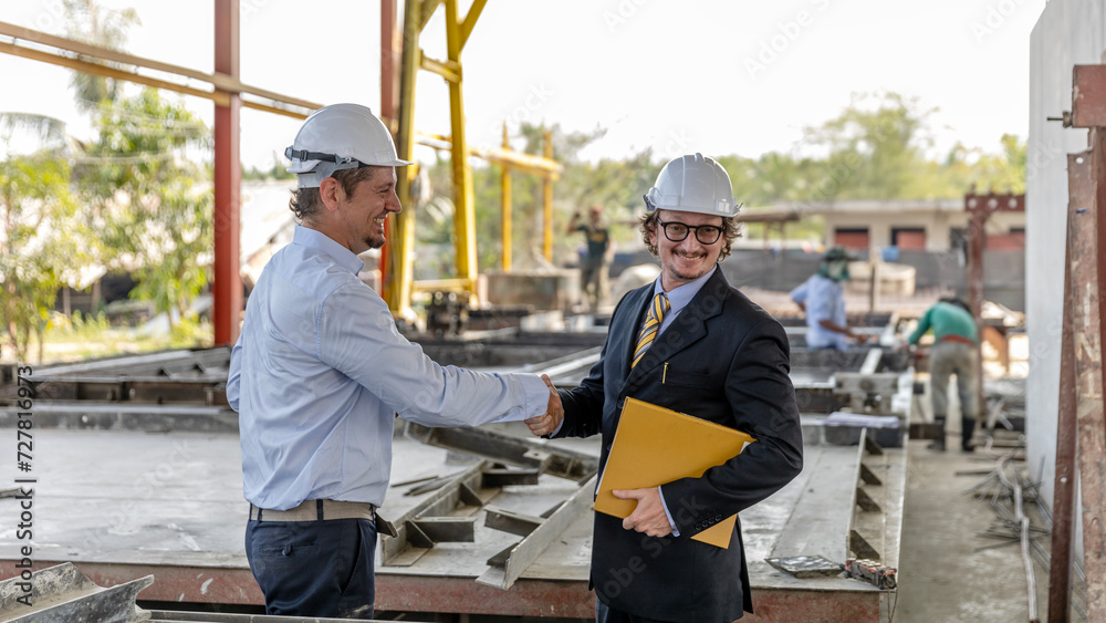 Two civil engineers from different cultures reach partnership agreement and have handshake in a construction factory