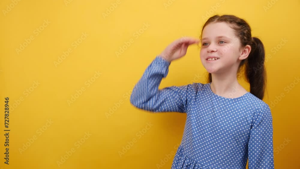 Portrait of adorable little girl kid 8-9 years old in blue dress hold hand at forehead looking far away distance, posing isolated on yellow color background wall in studio. Childhood lifestyle concept Portrait of adorable little girl kid 8-9 years old in blue dress hold hand at forehead looking far away distance, posing isolated on yellow color background wall in studio. Childhood lifestyle concept