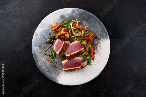 Traditional Japanese gourmet tuna fish steak tataki with vegetable slices and soy sprouts with sweet dour sauce served as top view on a Nordic design plate with copy space  photo