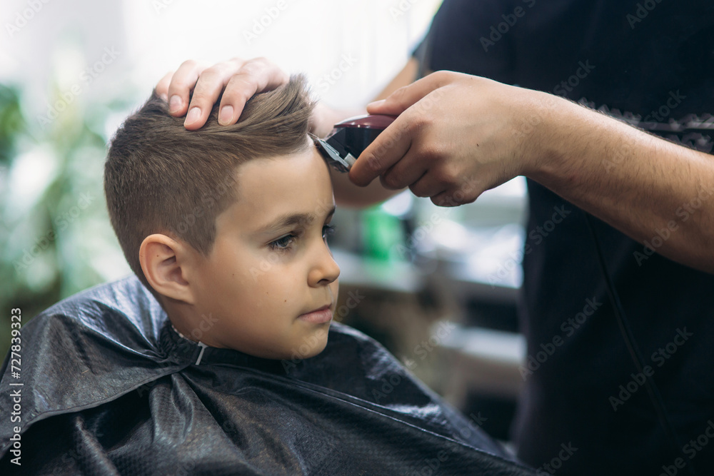 Professional hairdresser uses a hair clipper for fringing hair for a small boy Professional hairdresser uses a hair clipper for fringing hair for a small boy