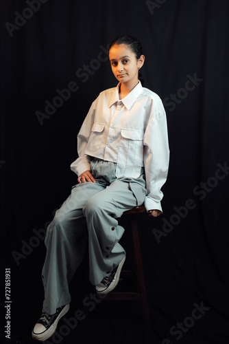 Obraz na płótnie A studio shot of 13 years old fashionable girl sitting on the chair in front of black background and posing for camera w salonie