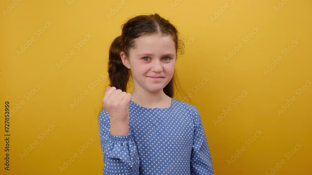 Portrait of excited pretty little girl child 8-9 years old wearing blue dress do winner gesture clench fist, posing isolated over yellow color background wall in studio. Childhood lifestyle concept Portrait of excited pretty little girl child 8-9 years old wearing blue dress do winner gesture clench fist, posing isolated over yellow color background wall in studio. Childhood lifestyle concept