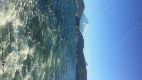 Rear view of Koryaksky volcano rising over Petropavlovsk-Kamchatsky city from boat sailing on Avacha bay ina sunny summer day. Real time handheld vertical video. Beauty in nature theme. photo