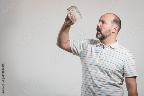 Surprised Caucasian man staring at empty beer glass, white background. Conceptual image of The Dry Challenge