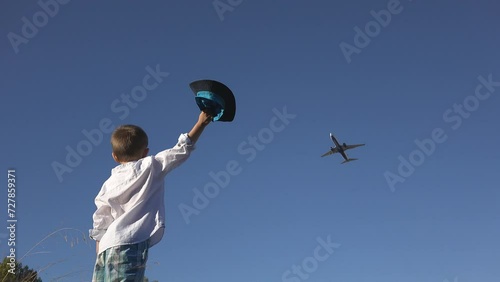 Little boy waving his hat to the airplane flying over