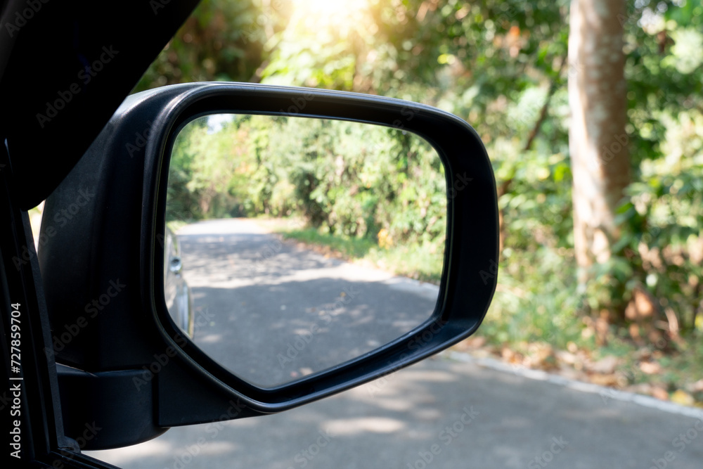 Rear view mirror of car on asphalt road background. Copy space and blurred of green forest at day time.