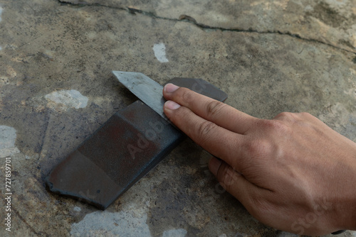 Knife sharpening on knife sharpening stone. Background of cement floor and hand holding knife sharpening.