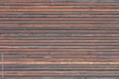 Fine brown wood paneling on the exterior wall of a building. The timber boards are mounted as a house facade. The full frame texture can be an abstract background.