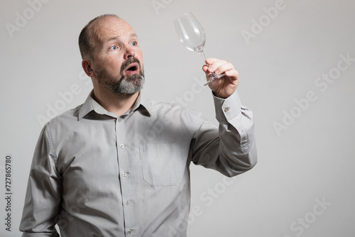 Surprised Caucasian man staring at empty wine glass, white background. Conceptual image of The Dry Challenge